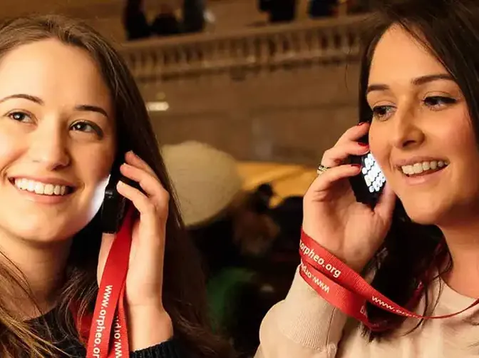 Twee bezoekers luisteren lachend naar een Orpheo Mikro audioguide